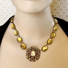 Load image into Gallery viewer, Yellow and gold necklace with a large decorative focal on a mannequin against a patterned wall.