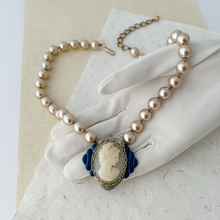 Load image into Gallery viewer, shell cameo necklace on blue and silver coloured frame with champagne coloured pearls displayed on a cream gloved hand