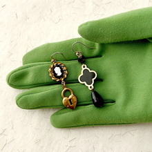 Load image into Gallery viewer, asymmetric black and gold earrings with cameo displayed on a green gloved hand