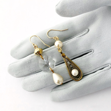Load image into Gallery viewer, asymmetric earrings in gold and pearl tones with chandelier crystal displayed on a gloved hand