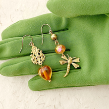 Load image into Gallery viewer, Gold earrings with golden peach beads, gold filigree and dragonfly charm on a green gloved hand