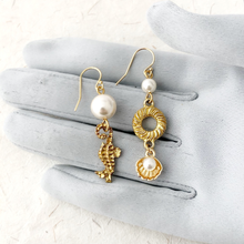 Load image into Gallery viewer, asymmetric gold earrings with pearl beads, seahorse and shell charms displayed on a grey gloved hand
