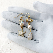 Load image into Gallery viewer, asymmetric earrings with starfish charm, vintage beads and evil eye connector displayed on a grey gloved hand