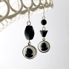 Load image into Gallery viewer, Earrings with black and white cameos, black beads and silver findings hanging from a white frame
