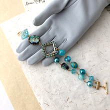 Load image into Gallery viewer, Aqua beaded bracelet on a gray gloved hand against a textured surface
