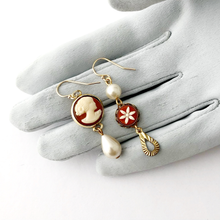 Load image into Gallery viewer, asymmetric vintage cameo earrings with pearls displayed on a grey gloved hand against a white background