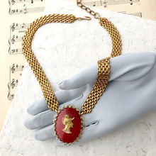 Load image into Gallery viewer, Gold chain necklace with red cameo focal displayed on a gloved hand against a sheet music background