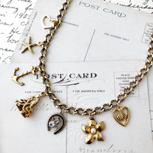 Load image into Gallery viewer, Gold charm necklace on a vintage postcard background