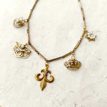 Load image into Gallery viewer, Gold toned necklace with unusual vintage charms on handmade paper background