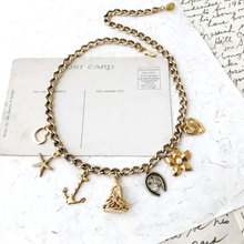 Load image into Gallery viewer, Gold necklace with various charms on vintage paper surface