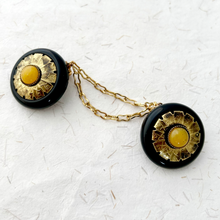 Load image into Gallery viewer, A gold and black cloak clasp or sweater clip on handmade paper background