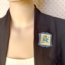 Load image into Gallery viewer, A close-up of a mannequin torso wearing a dark charcoal open-front jacket over a cream top, with a blue handmade brooch with a collage featuring vintage paper and a New Zealand stamp,