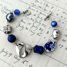 Load image into Gallery viewer, bracelet made with vintage and repurposed beads in blue and silver displayed on a antique ledger page