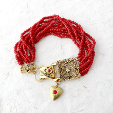 Load image into Gallery viewer, a red beaded bracelet with gold clasp and heart shaped locket against a neutral background