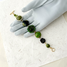 Load image into Gallery viewer, green toned bracelet made with vintage earrings and beads displayed on a grey gloved hand