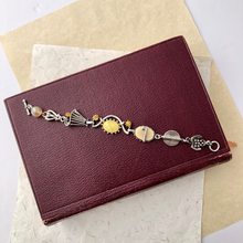 Load image into Gallery viewer, Bracelet with decorative silver and yellow themed elements on a maroon leather-bound book