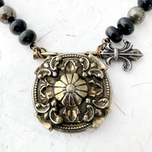 Load image into Gallery viewer, Necklace with ornate shield-like pendant and black and gold beads on a textured white background