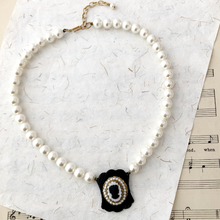 Load image into Gallery viewer, Pearl necklace with a vintage black and white cameo pendant on a textured surface with music sheet background