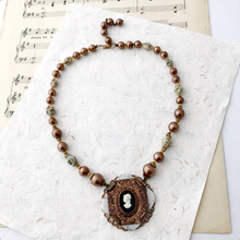 Load image into Gallery viewer, Necklace with a vintage cameo pendant and vintage beads on a textured paper background