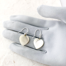 Load image into Gallery viewer, vintage heart-shaped mother of pearl earrings on a gray gloved hand