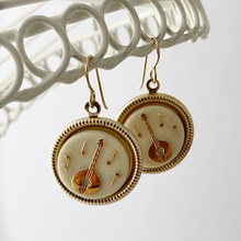 Load image into Gallery viewer, Pair of earrings with banjo and musical design hanging from a white frame against a white background