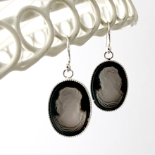 Load image into Gallery viewer, Black and white glass cameo earrings hanging on a white frame.