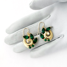 Load image into Gallery viewer, vintage gold toned swirled earrings set with green rhinestones displayed on a grey gloved hand