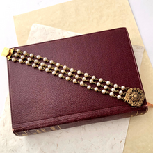 Load image into Gallery viewer, Pearl bracelet with a gold-toned filigree clasp on a maroon book