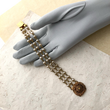 Load image into Gallery viewer, Pearl bracelet with a gold-toned filigree clasp displayed on a grey loved hand