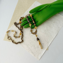Load image into Gallery viewer, long bead and chain necklace in caramel colours with mother-of-pearl pendant displayed on a green gloved hand and paper background