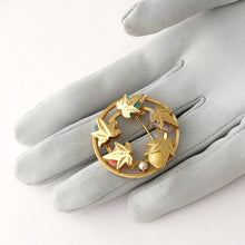 Load image into Gallery viewer, sarah coventry circle brooch set with coloured agates nestled under gold leaves and with a cultured pearl. displayed on a gloved hand