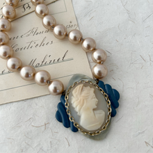 Load image into Gallery viewer, close up of shell cameo necklace on blue and silver coloured frame with champagne coloured pearls
