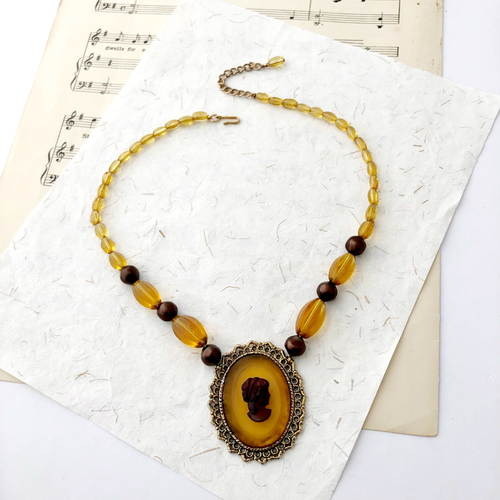 Necklace with amber-colored beads and cameo pendant on a textured paper background
