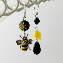 Load image into Gallery viewer, A pair of handmade earrings displayed on a white wire frame. They feature silver ear-wires, beads in yellow and black with a bee charm with rhinestone wings.
