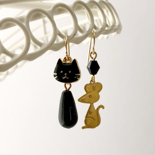 asymmetric earring with a black cat and brass mouse hanging from a white frame