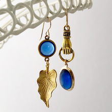 Load image into Gallery viewer, asymmetric earrings in blue and gold hanging from a white frame
