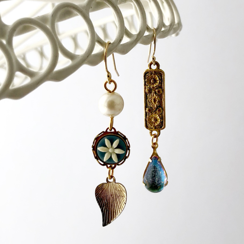 Asymmetric earrings with vintage floral and leaf designs hanging against a white background