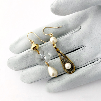 asymmetric earrings in gold and pearl tones with chandelier crystal displayed on a gloved hand