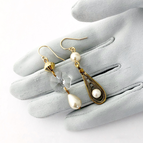 asymmetric earrings in gold and pearl tones with chandelier crystal displayed on a gloved hand
