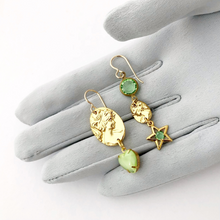 Load image into Gallery viewer, asymmetric earrings with gold metal cameos, green heart shaped rhinestone and star charm on a gloved hand
