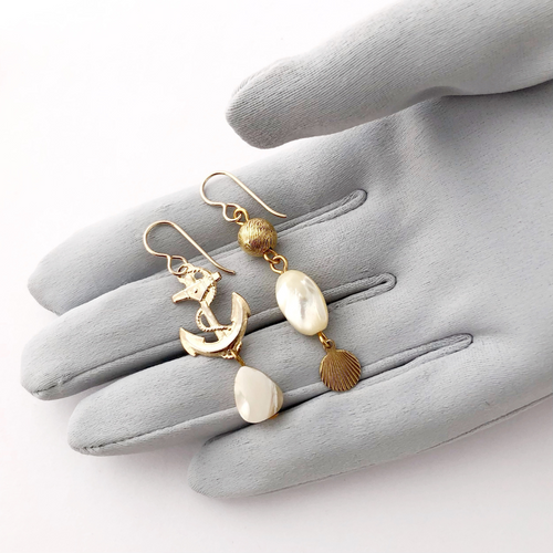 earrings with an anchor and mother of pearl beads on a gloved hand