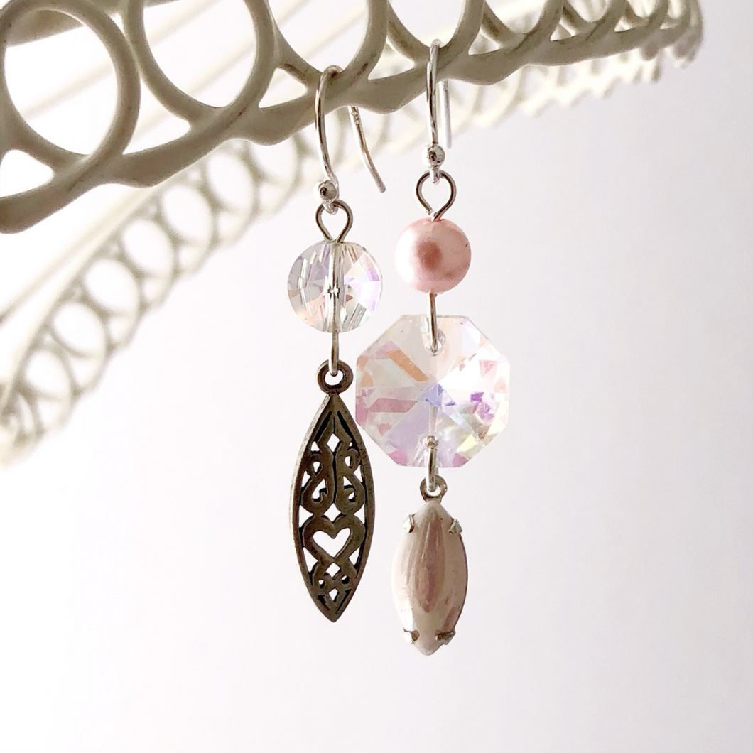 asymmetric earrings in pink and silver hanging from a white frame