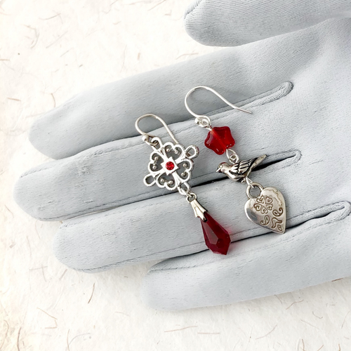 Silver and red asymmetric earrings displayed on a grey gloved hand