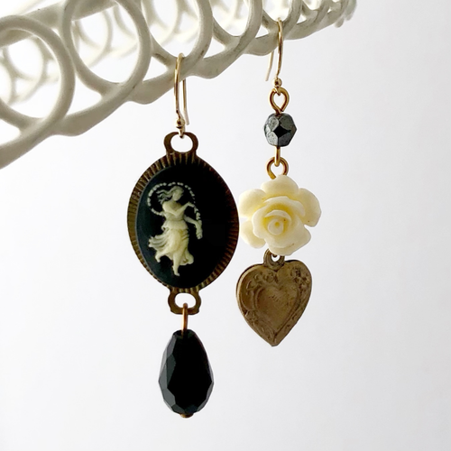 asymmetrical earrings with vintage black and cream cameo vintage cream flower, heart charm and beads hanging against a white background