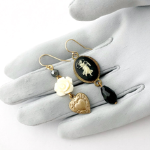Load image into Gallery viewer, asymmetrical earrings with vintage black and cream cameo vintage cream flower, heart charm and beads  on a grey gloved hand
