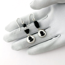 Load image into Gallery viewer, Earrings with black and white cameos, black beads and silver findings on a grey gloved hand
