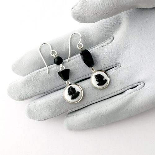 Earrings with black and white cameos, black beads and silver findings on a grey gloved hand