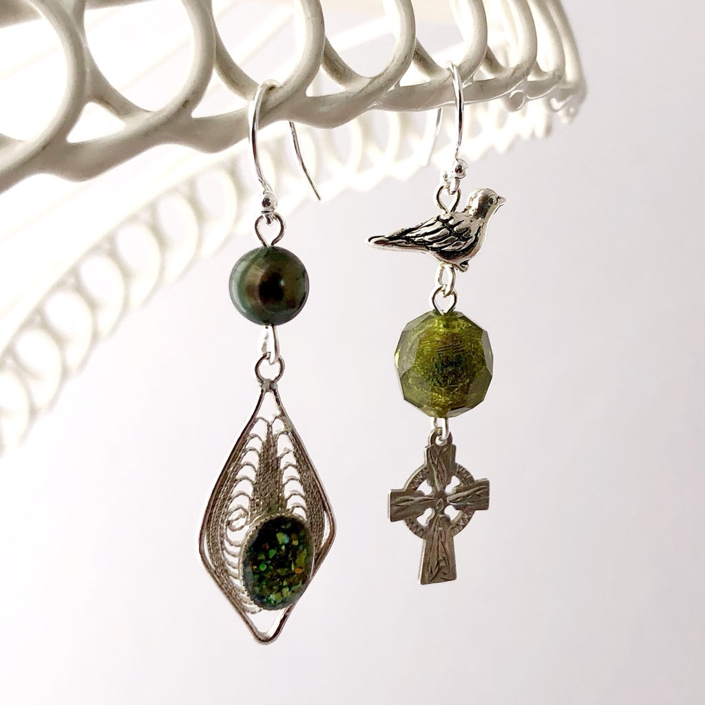 asymmetric earrings in silver and bronze green colours hanging from a white wire lace frame