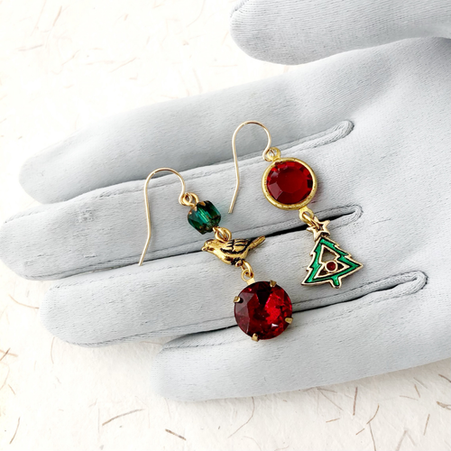 Asymmetric Christmas themed earrings displayed on a grey gloved hand