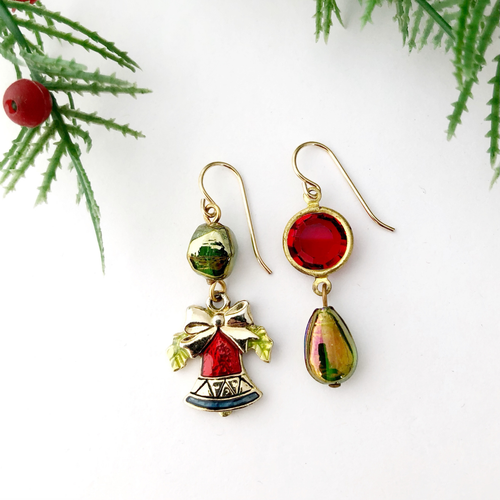 Pair of festive earrings with red and green accents on a white background with Christmas tree branches.